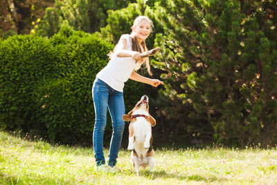 Full length of teenage girl playing with dog against trees