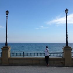 Rear view of woman standing by railing against sea