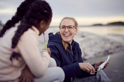 Cheerful young mother removing toothpaste on toothbrush while sitting by daughter