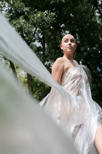 Naked woman covered in plastic standing at forest