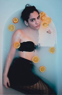 High angle portrait of young woman lying in bathtub with slices of citrus fruit floating on water