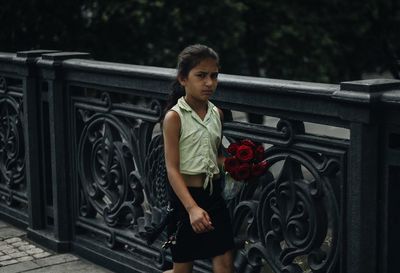Portrait of girl holding red roses walking by railing