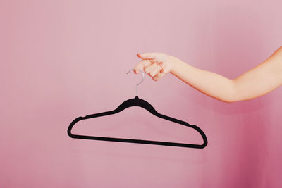 Woman holding black hanger. studio photo with light pink background.