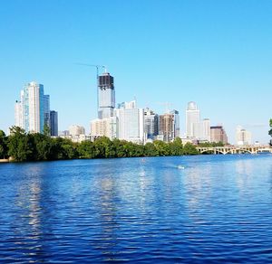 Sea by buildings in city against clear blue sky