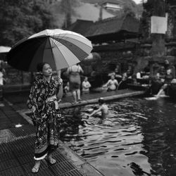 Woman holding umbrella while standing by pond during rainy season