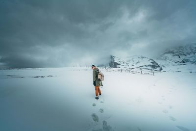 Rear view of person standing on snowcapped mountain against sky