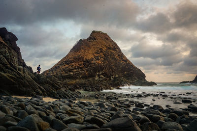 Man standing on rock by sea against sky