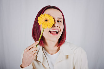 Studio portrait millennial woman with bright red color hair and yellow flower.