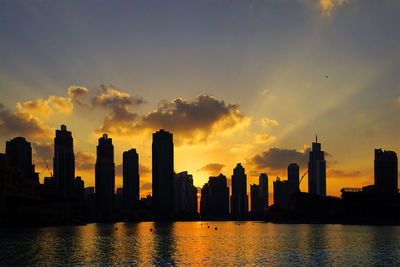 Silhouette city by river against sky during sunset