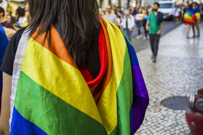 Rear view of woman with rainbow flag standing on street