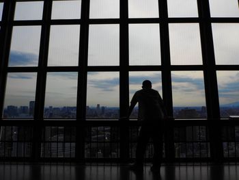 Rear view of silhouette man standing in balcony seen through window