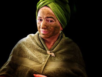 Portrait of woman with facial mask against black background