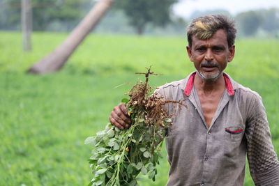 Man holding plant while standing on field