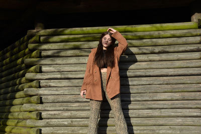 A young woman with a brown coat, posing in front of old wooden planks