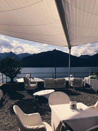 Chairs and tables and lounge chair by sea against sky