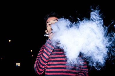 Young man smoking cigarette against black background