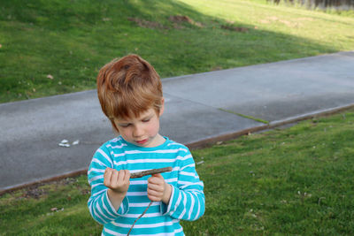 The blond boy holds sticks in his hands and examines them carefully. a five-year-old thoughtful boy.