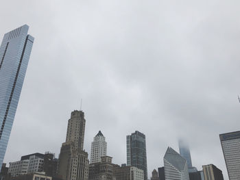 Low angle view of modern buildings against cloudy sky in city