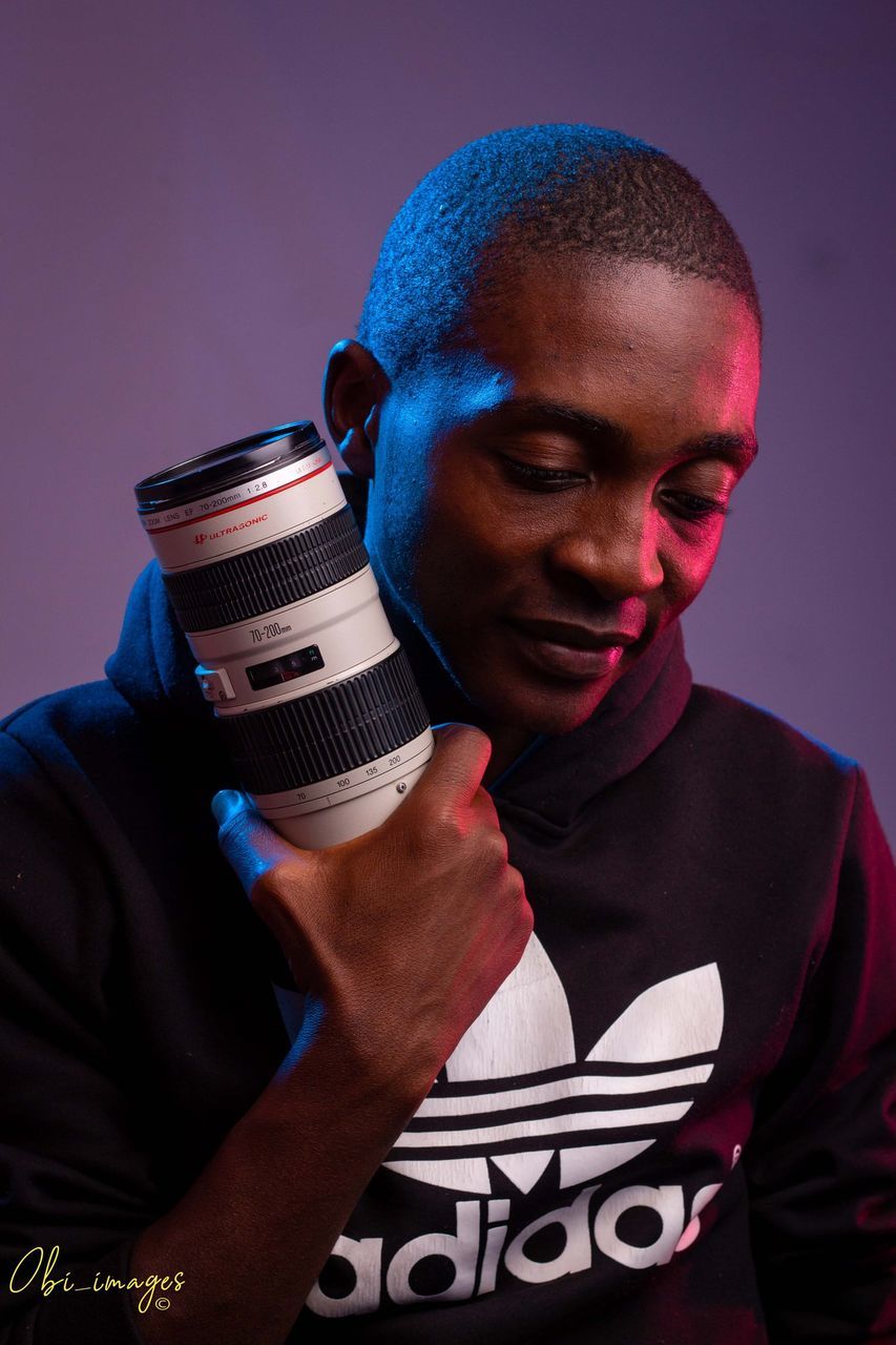 PORTRAIT OF YOUNG MAN HOLDING CAMERA OVER GRAY BACKGROUND