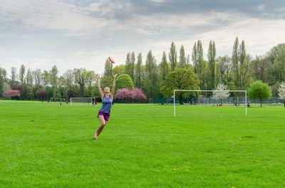 Mid adult woman with arms raised catching plastic disc on field
