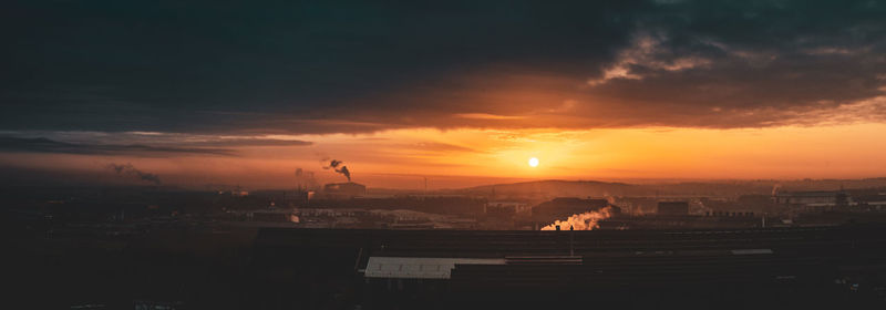 Silhouette of buildings against cloudy sky during sunset