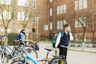 Boys talking on mobile phone by bicycle parking area outside school building