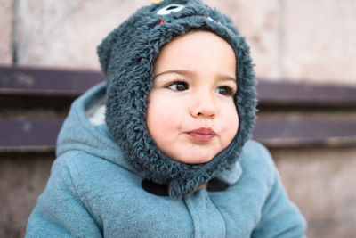 Close-up of cute baby boy in warm clothing looking away while sitting against wall