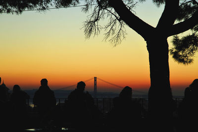 Silhouette people at miradouro da graca against april 25th bridge during sunset