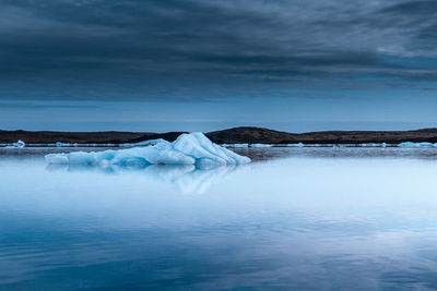 Iceberg floating in sea against sky at dusk