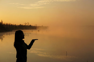 Rear view of silhouette woman standing against sky during sunset