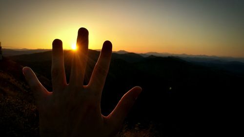 Cropped hand gesturing against sky during sunset