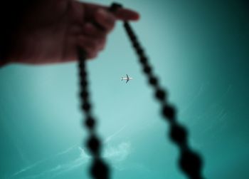 Airplane seen through bead necklace held by man