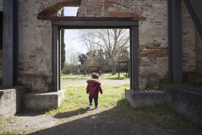 Rear view of baby boy walking on grassy field at old ruin