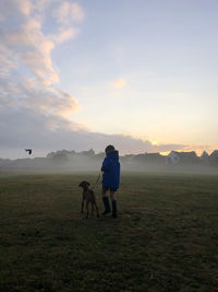 Rear view of friends standing on field against sky during sunset