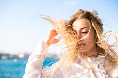 Close-up of beautiful woman with tousled hair against clear sky