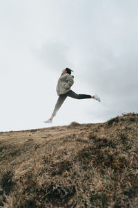 Low angle view of woman jumping on grassy field against sky