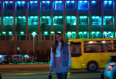 Portrait of young woman standing in illuminated city at night