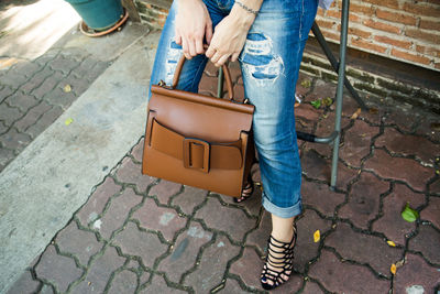 Low section of woman holding bag while standing on footpath