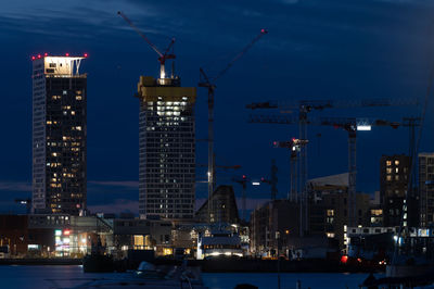 Illuminated modern buildings in city against sky at dusk