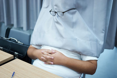 Midsection of person hiding behind curtain with eyeglasses