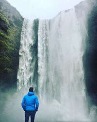 Rear view of man looking at skogafoss waterfall