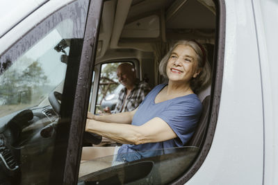 Smiling senior woman driving motor home with man during road trip