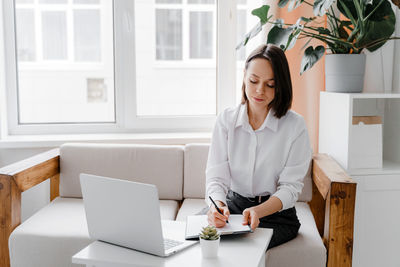 Businesswoman writing while sitting on sofa at home