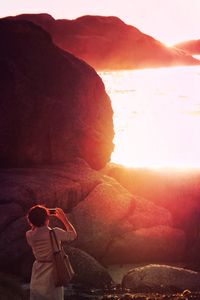 Woman photographing sea by rock formations on sunny day