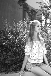 Young woman smiling while sitting on bench by plants