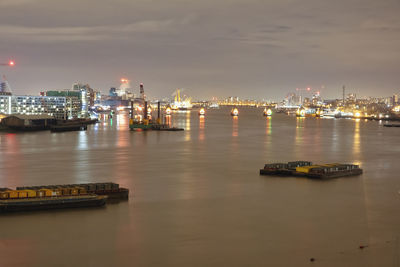 Illuminated buildings by river against sky in city at night