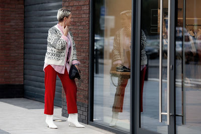 Fashionably dressed woman shopping, looking at reflection in mirror of shop window outside