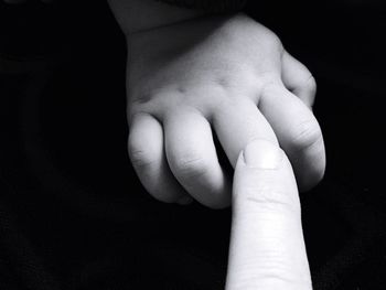 Cropped finger touching child hand against black background