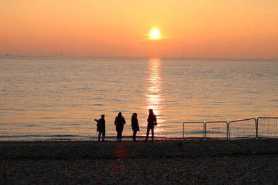 Silhouette people standing at beach during sunset