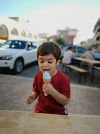 Cute boy eating ice cream on sidewalk